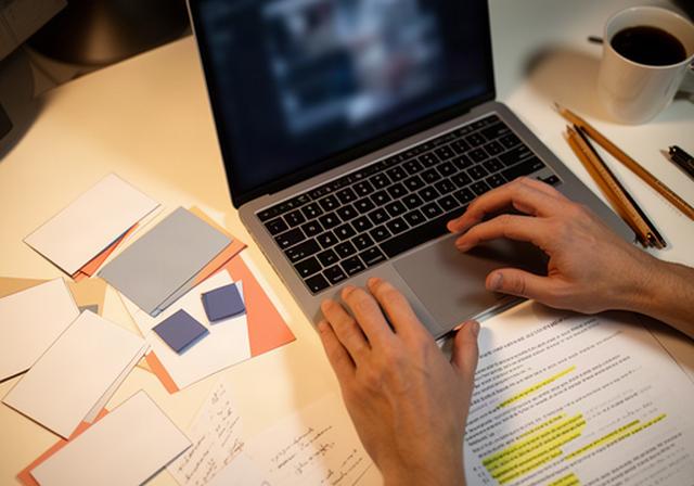 Schreibende Hände an einem Laptop mit Szenenplan, Notizen und markiertem Drehbuch